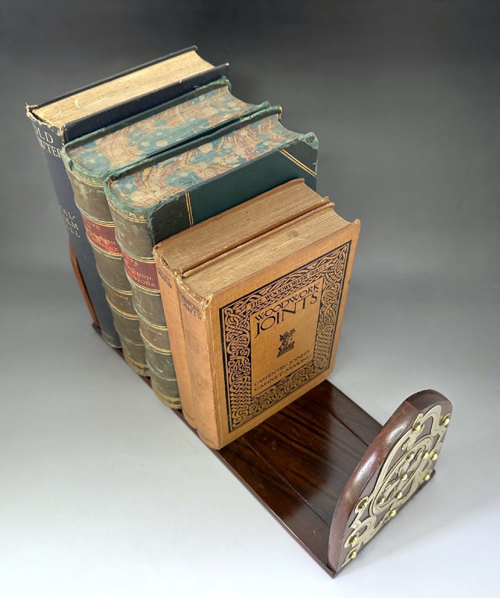 An extended wooden Victorian book slide with brass strapwork end panels holding a row of antique books. View VII