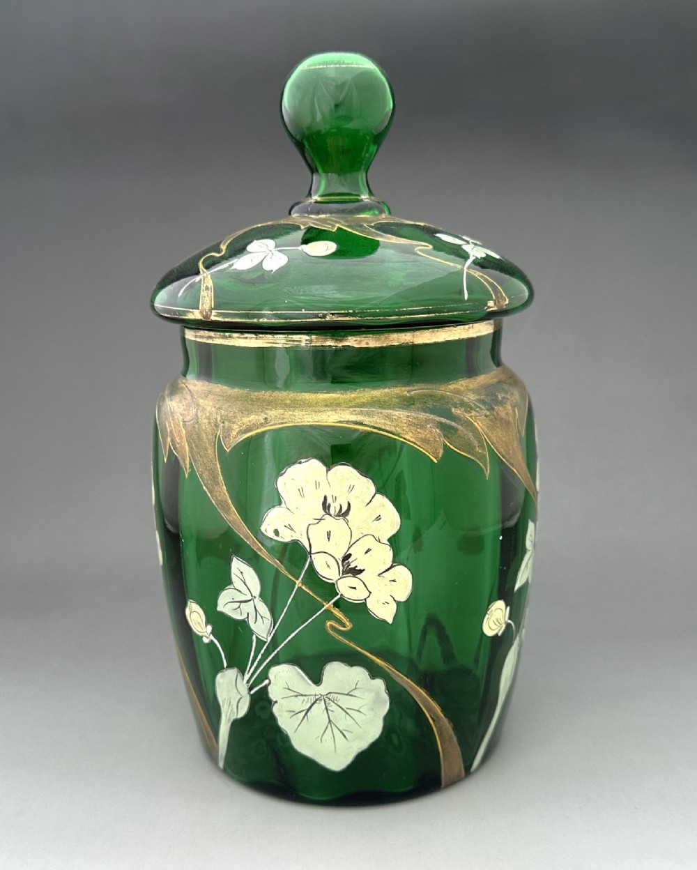A green glass biscuit barrel featuring hand-painted white floral enamel and gold gilded leaf motifs with a matching glass lid. View III