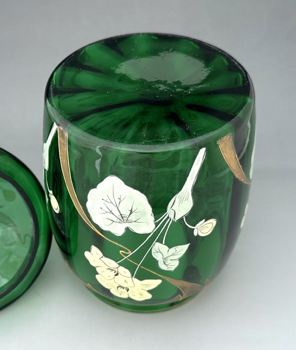 A green glass biscuit barrel featuring hand-painted white floral enamel and gold gilded leaf motifs with a matching glass lid. View VI