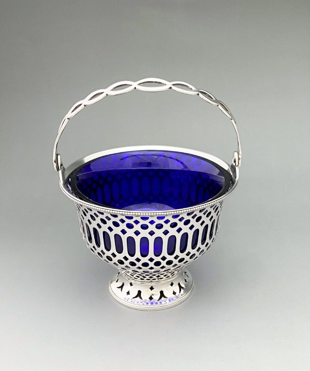 A pierced sterling silver swing-handled sugar basket featuring geometric openwork and a dark blue glass liner. View II