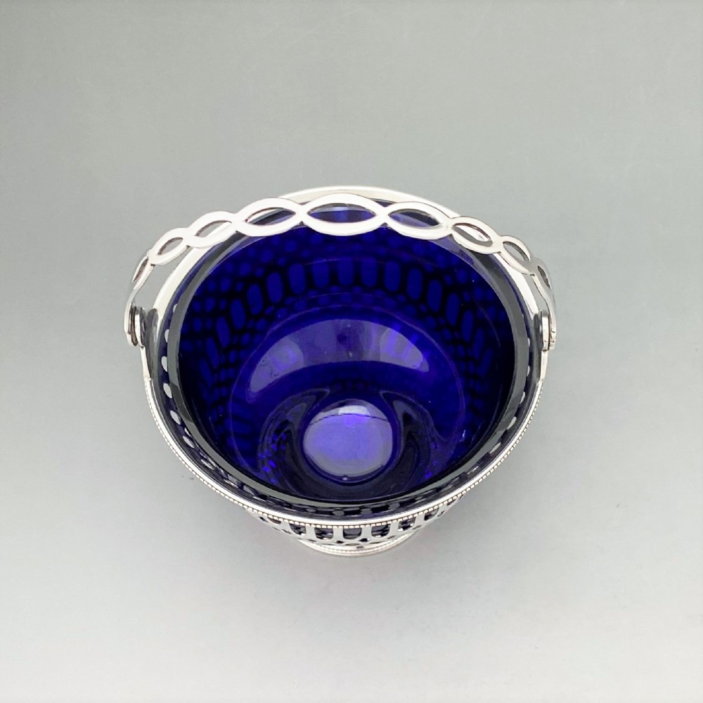 A pierced sterling silver swing-handled sugar basket featuring geometric openwork and a dark blue glass liner. View III