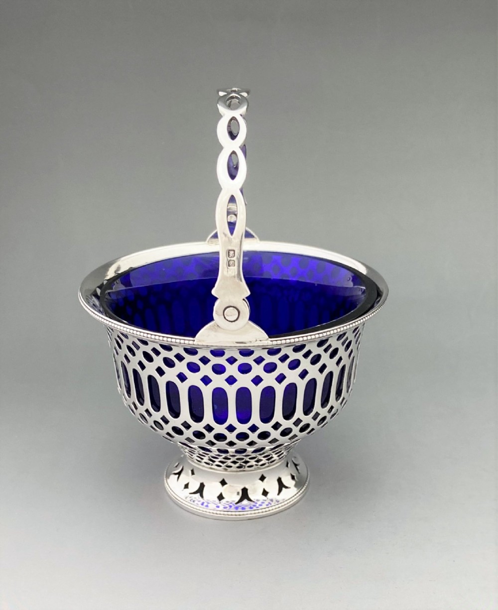 A pierced sterling silver swing-handled sugar basket featuring geometric openwork and a dark blue glass liner. View IV