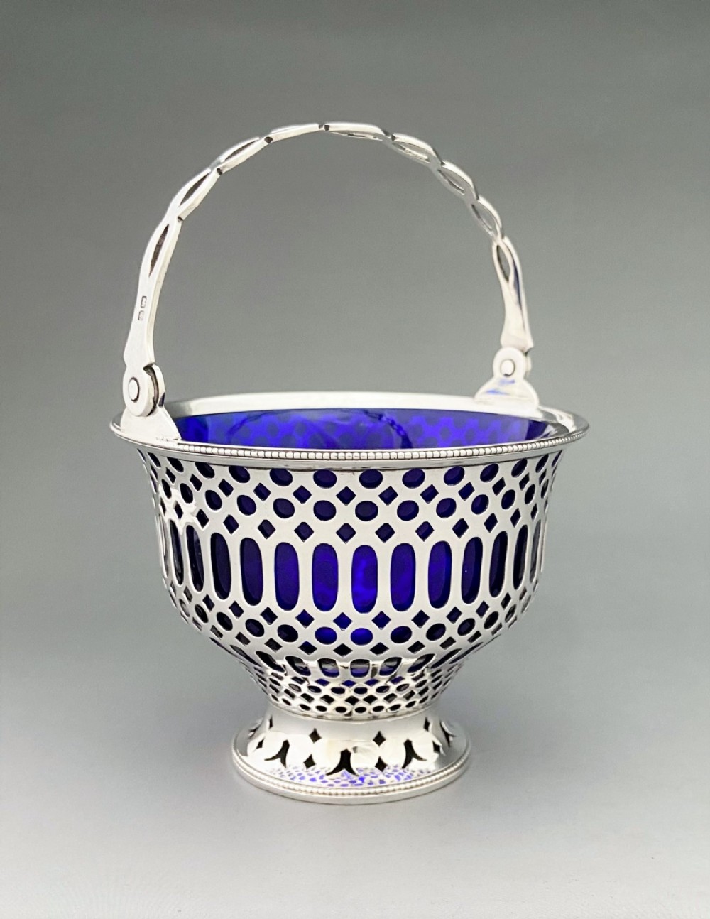 A pierced sterling silver swing-handled sugar basket featuring geometric openwork and a dark blue glass liner.