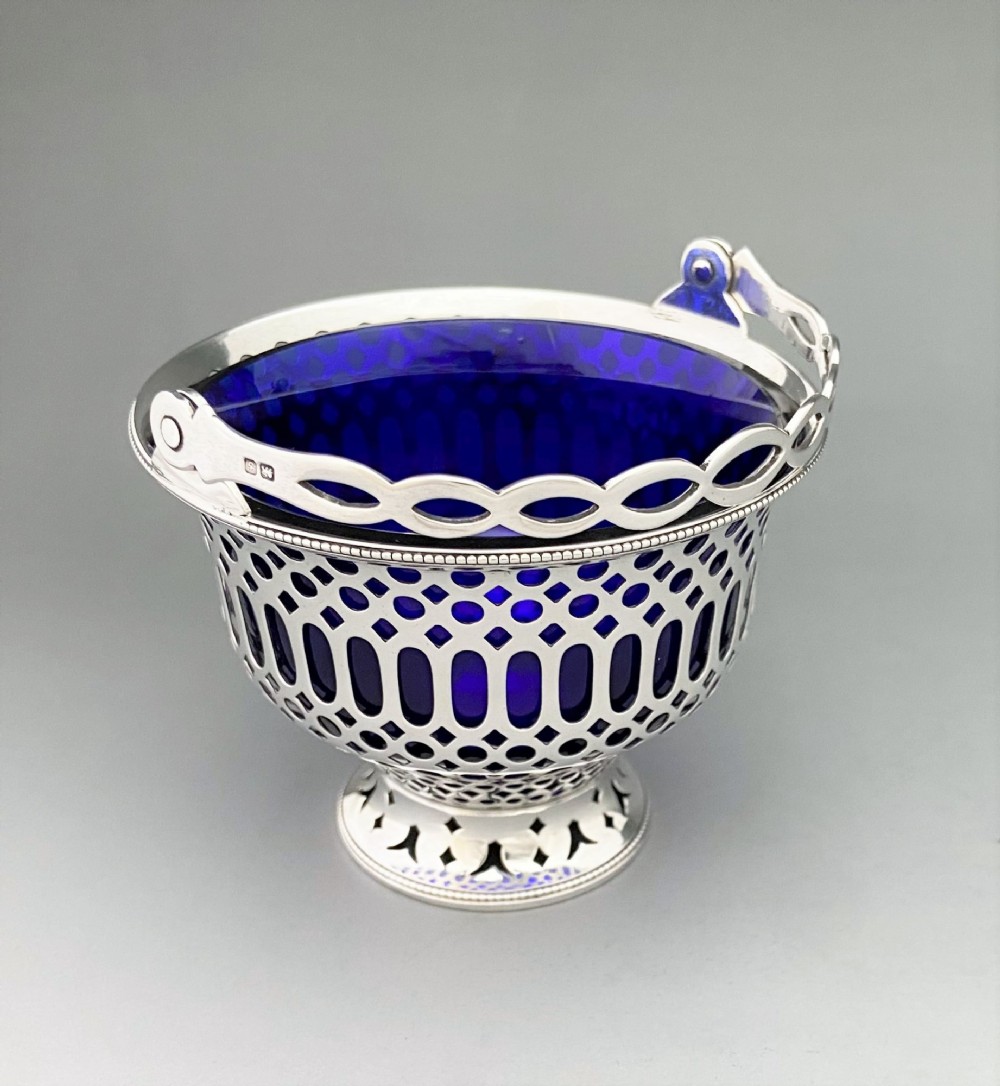 A pierced sterling silver swing-handled sugar basket featuring geometric openwork and a dark blue glass liner. View V