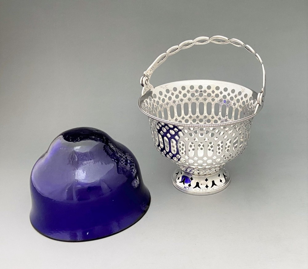 A pierced sterling silver swing-handled sugar basket featuring geometric openwork and a dark blue glass liner. View VI