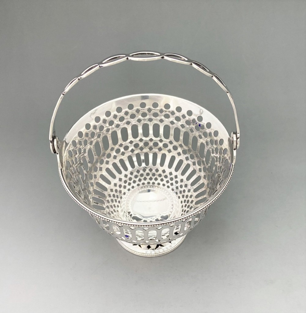 A pierced sterling silver swing-handled sugar basket featuring geometric openwork and a dark blue glass liner. View VII