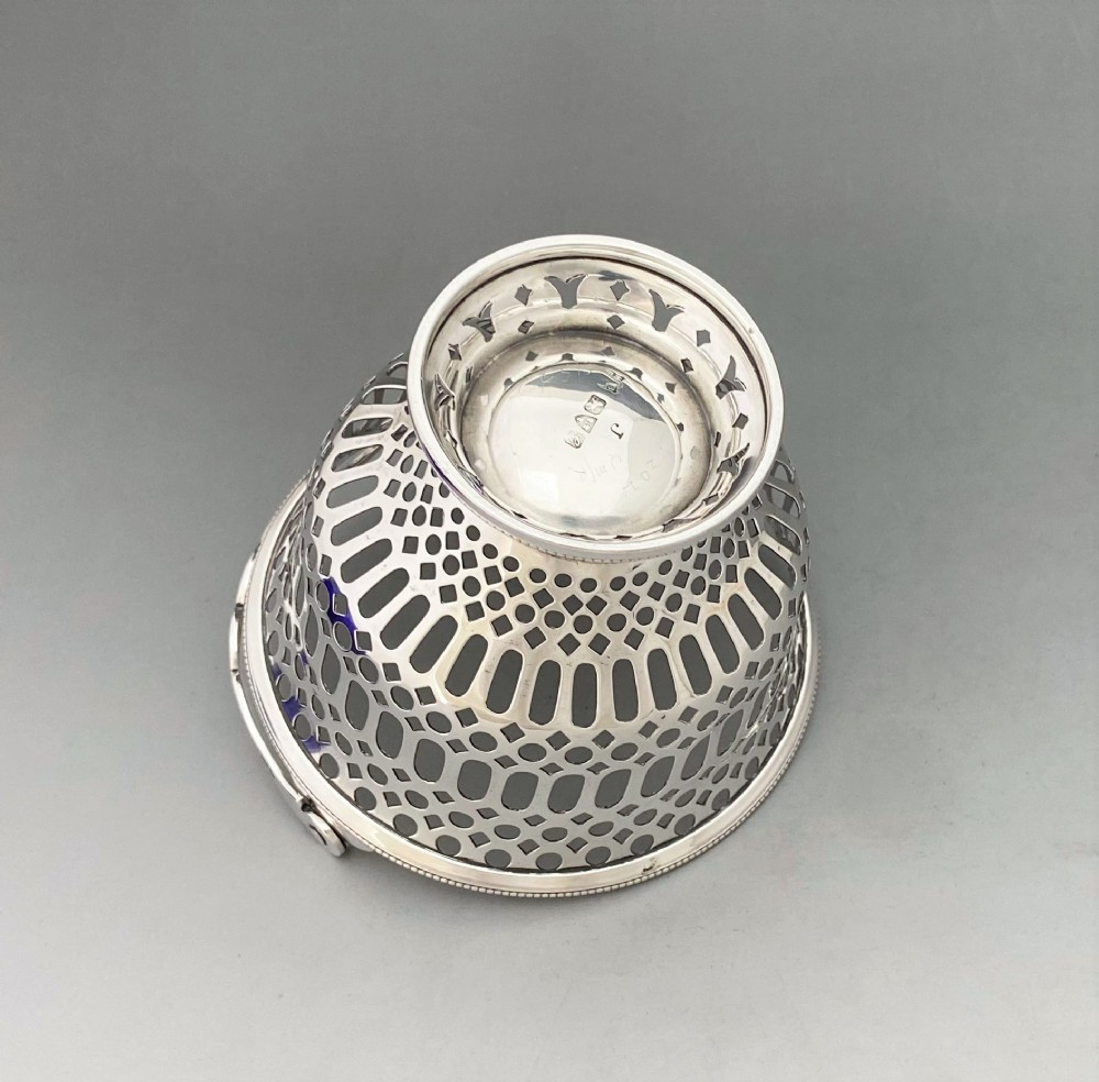 A pierced sterling silver swing-handled sugar basket featuring geometric openwork and a dark blue glass liner. View VIII