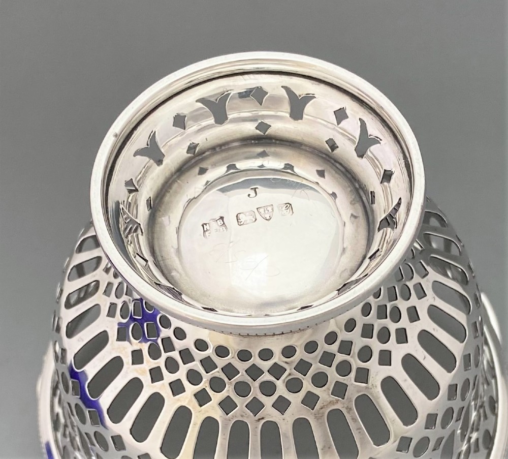 A pierced sterling silver swing-handled sugar basket featuring geometric openwork and a dark blue glass liner. View IX