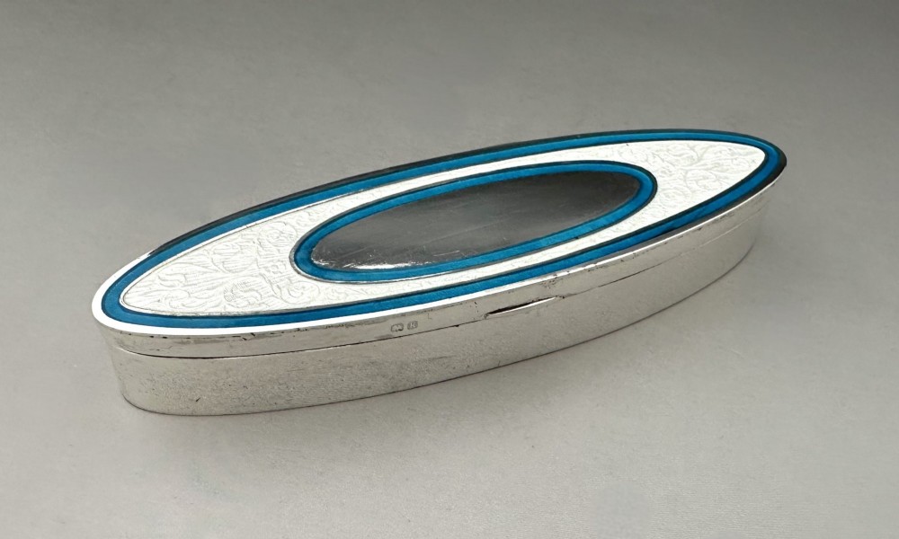 An elongated navette-shaped silver trinket box with concentric blue and white enamel borders over an engine-turned pattern.