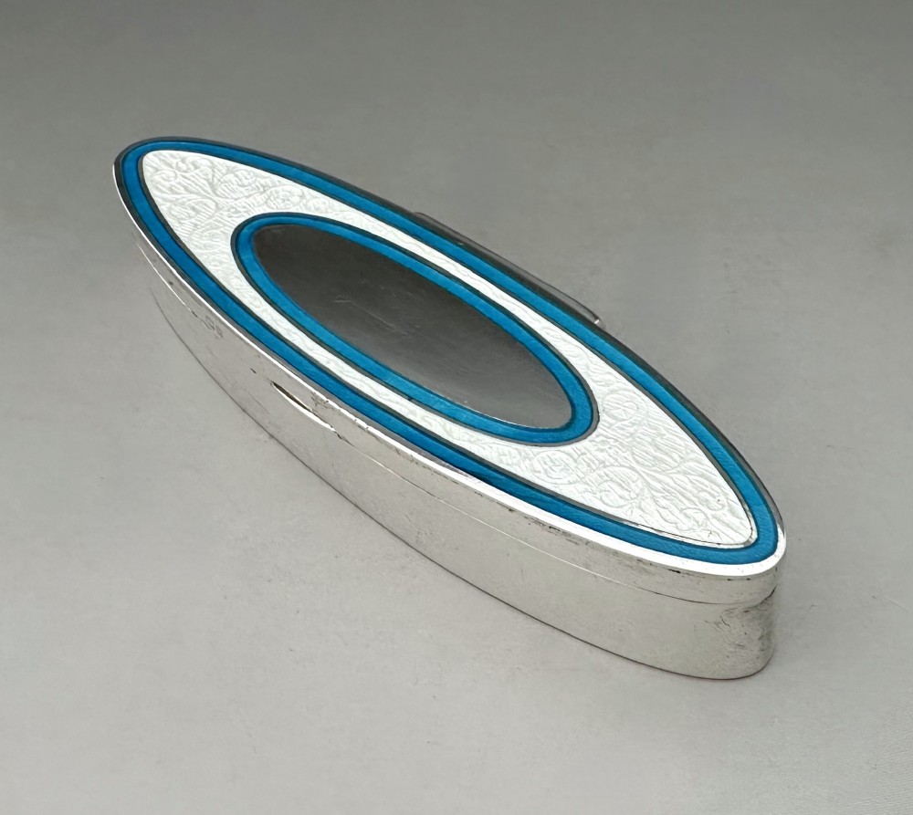 An elongated navette-shaped silver trinket box with concentric blue and white enamel borders over an engine-turned pattern. View IV