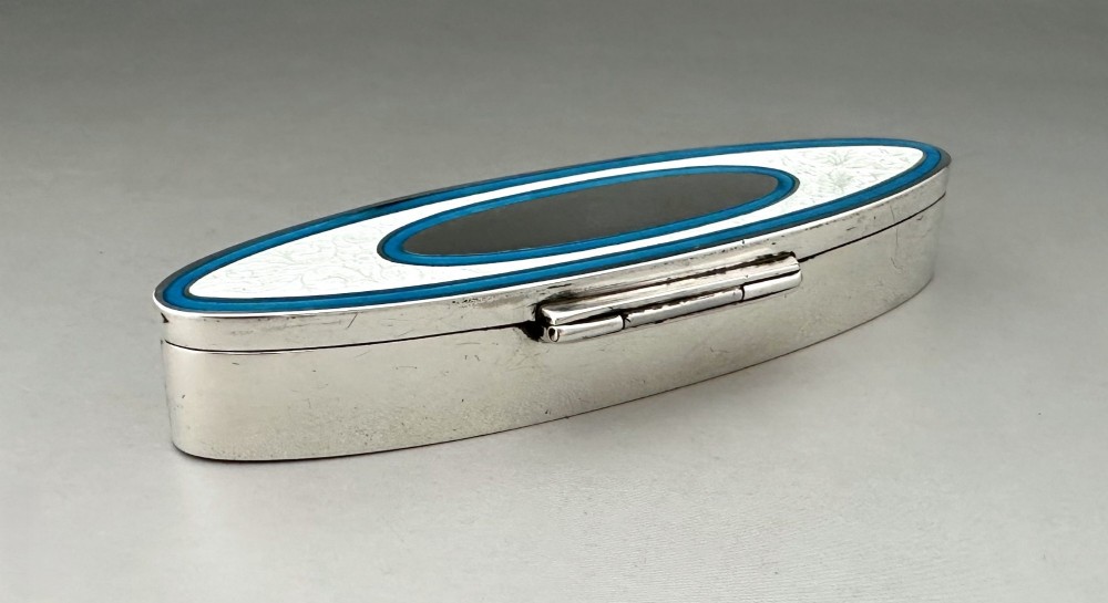 An elongated navette-shaped silver trinket box with concentric blue and white enamel borders over an engine-turned pattern. View V
