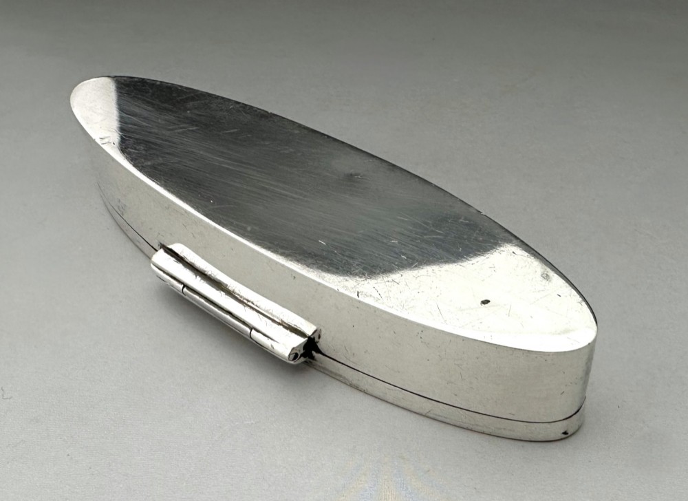 An elongated navette-shaped silver trinket box with concentric blue and white enamel borders over an engine-turned pattern. View VIII