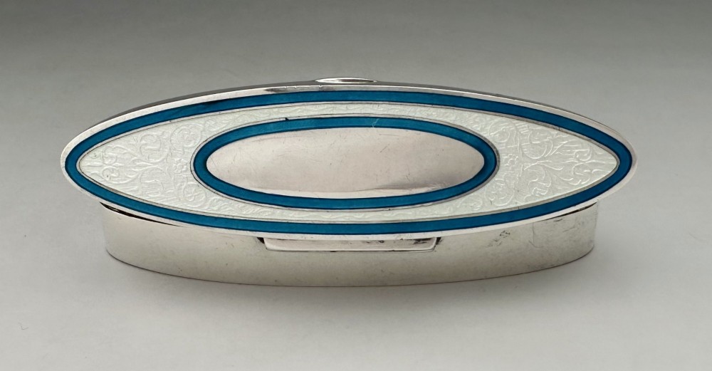 An elongated navette-shaped silver trinket box with concentric blue and white enamel borders over an engine-turned pattern. View IX