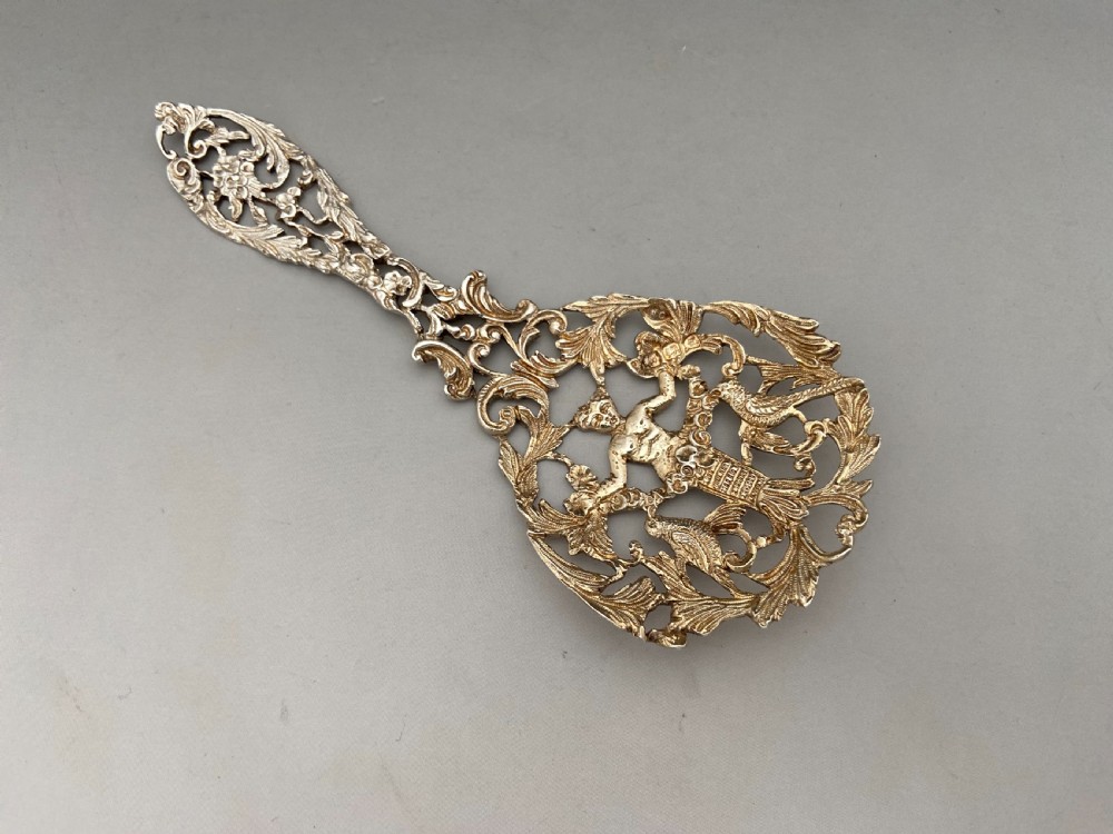 An ornate Victorian cast sterling silver bonbon spoon featuring intricate pierced scrollwork, foliage, and a cherub motif. View VII
