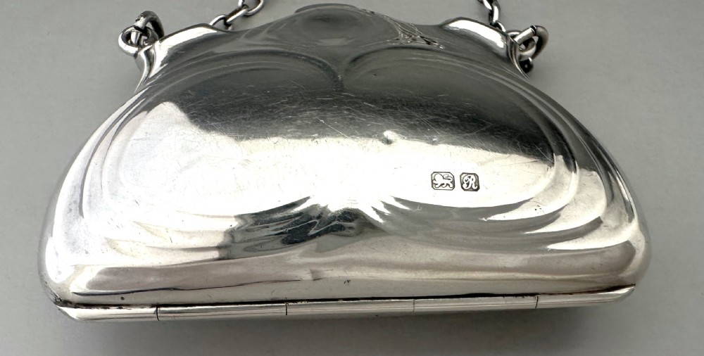 A George V sterling silver cocktail purse with a chain handle, finger ring, and British hallmarks stamped on the contoured front surface. View X