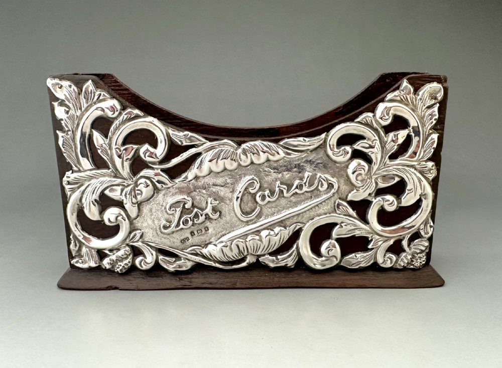 An Edwardian wooden postcard holder featuring an intricate repousse silver mount embossed with the words Post Cards.