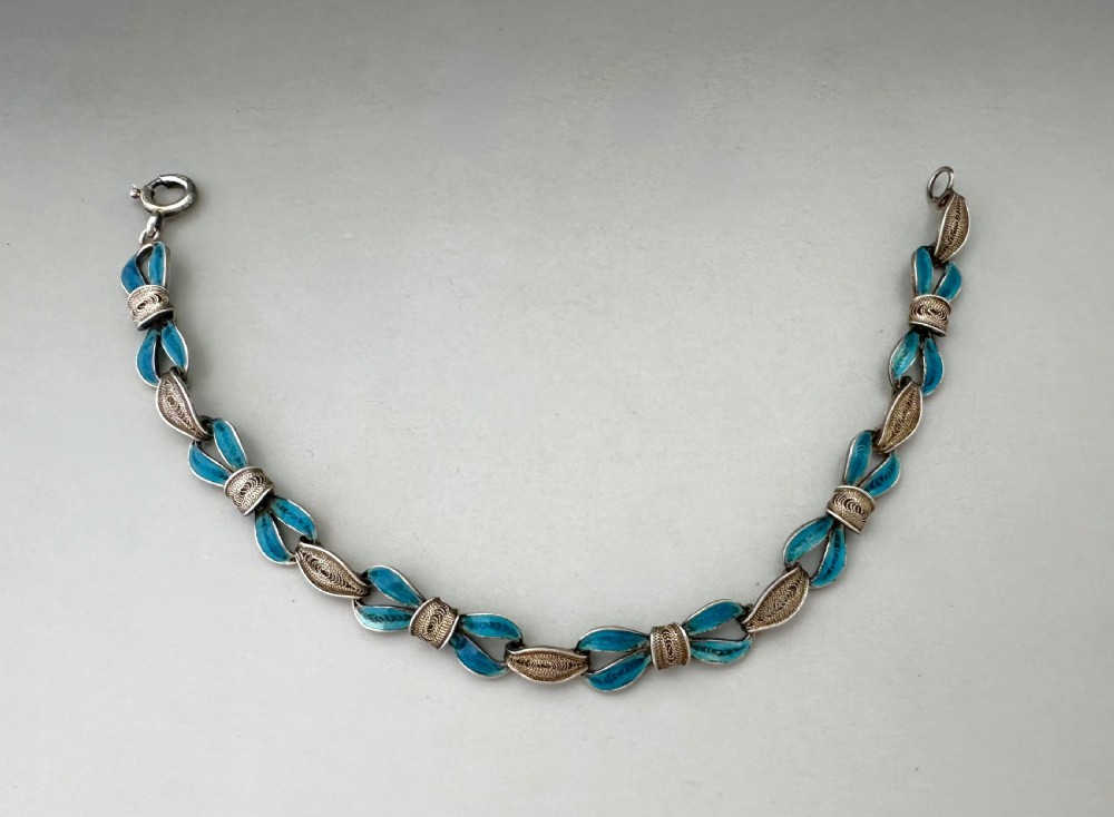 A silver filigree link bracelet featuring bow-shaped segments filled with turquoise blue enamel and secured with a bolt ring clasp. View VI