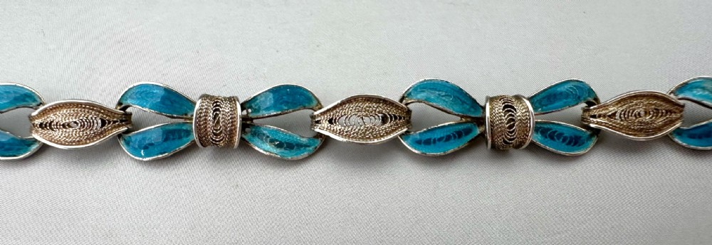 A silver filigree link bracelet featuring bow-shaped segments filled with turquoise blue enamel and secured with a bolt ring clasp. View III