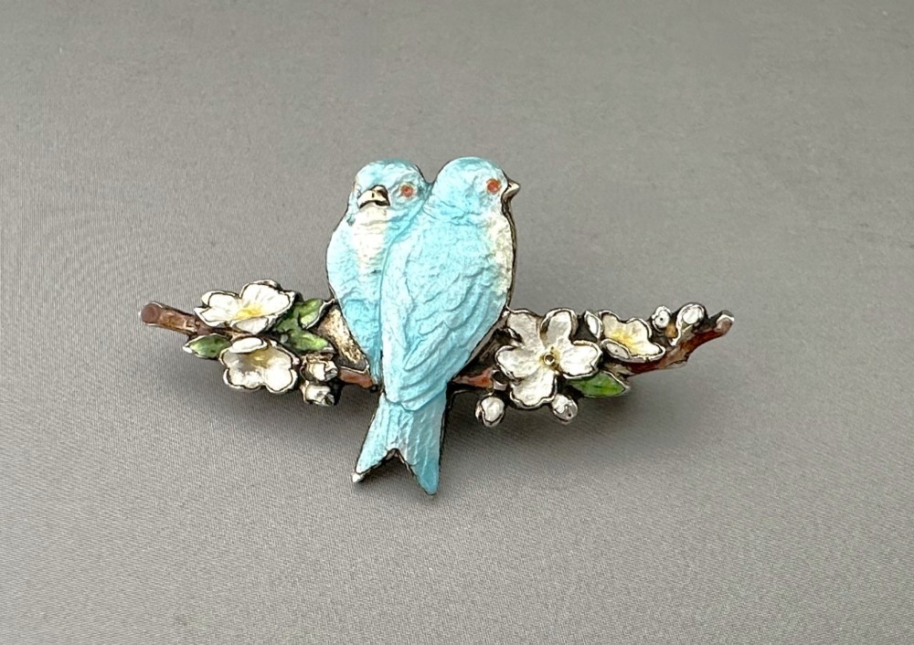A silver-gilt brooch depicting two light blue enamel birds perched on a flowering branch with white enamel blossoms. View II