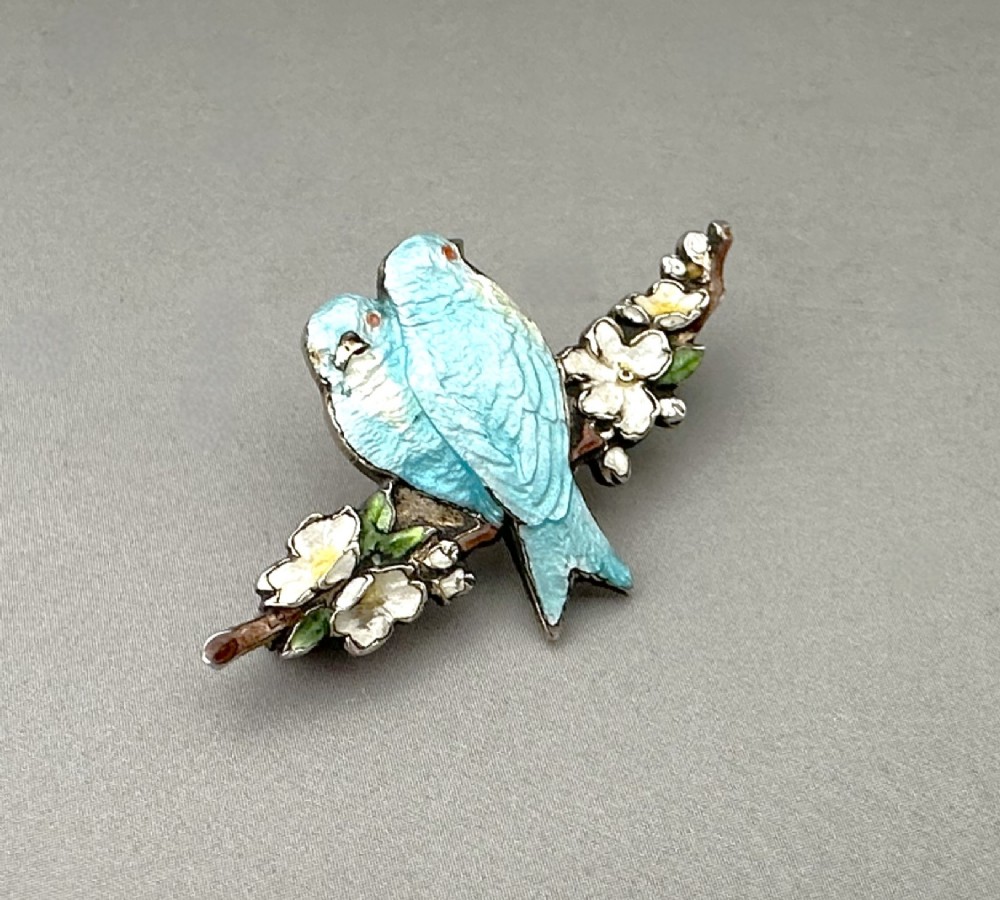 A silver-gilt brooch depicting two light blue enamel birds perched on a flowering branch with white enamel blossoms. View III