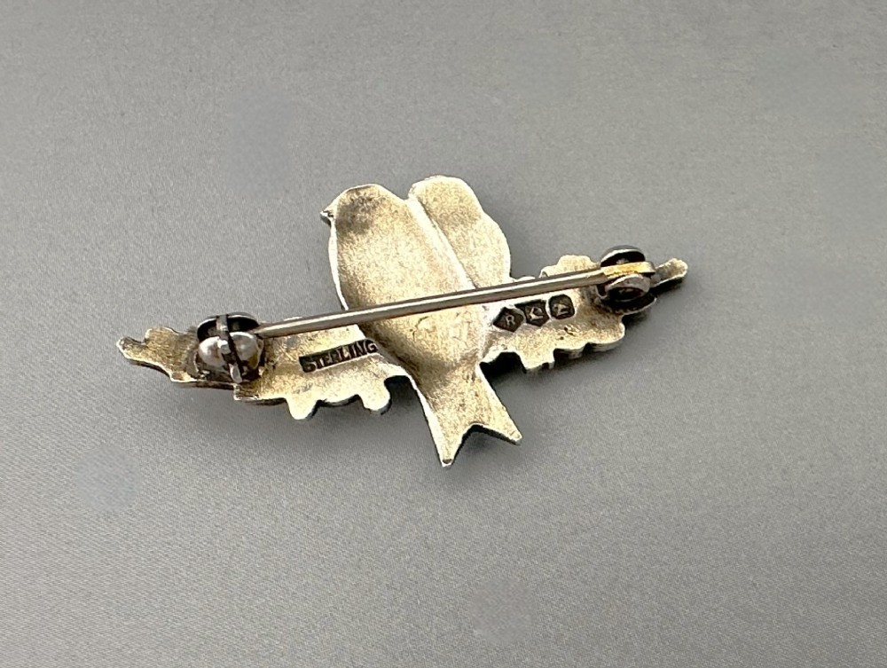 A silver-gilt brooch depicting two light blue enamel birds perched on a flowering branch with white enamel blossoms. View IV