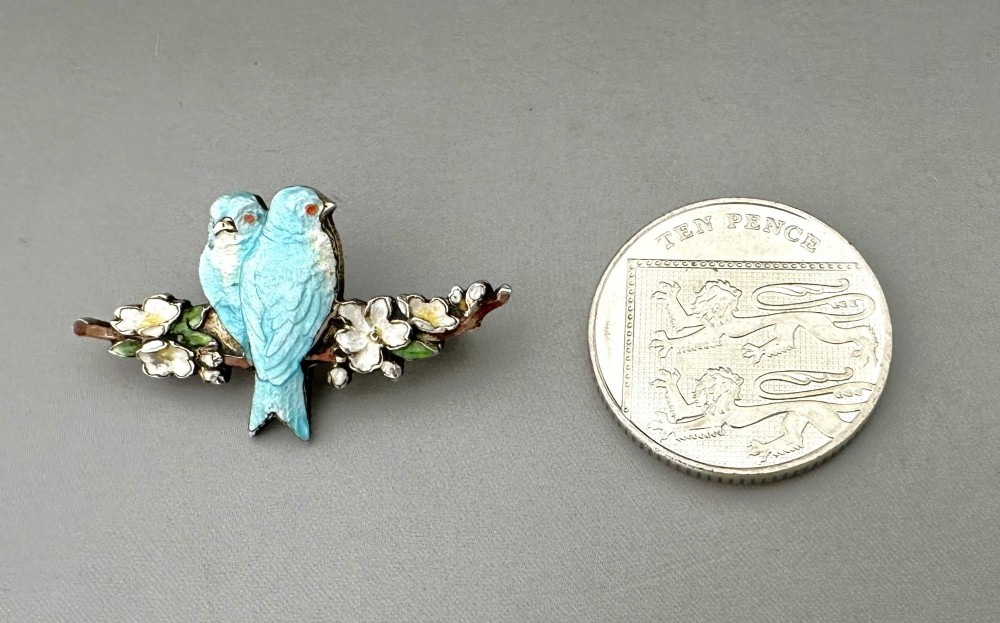 A silver-gilt brooch depicting two light blue enamel birds perched on a flowering branch with white enamel blossoms. View VI