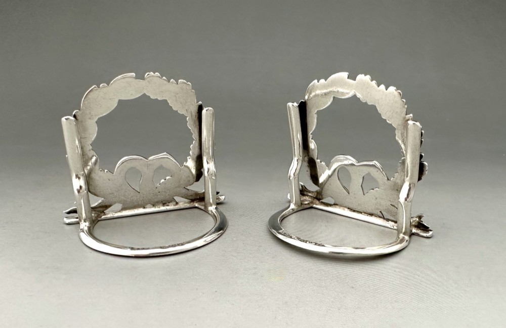 A pair of sterling silver menu card holders shaped as laurel and oak leaf wreaths tied with a ribbon bow on a flat base with rear support struts. View II