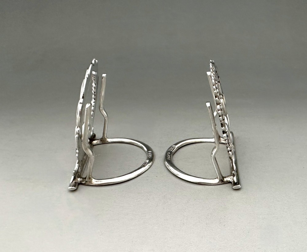 A pair of sterling silver menu card holders shaped as laurel and oak leaf wreaths tied with a ribbon bow on a flat base with rear support struts. View IV