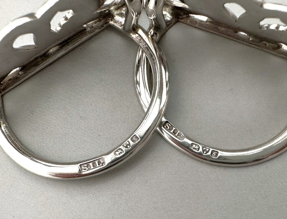 A pair of sterling silver menu card holders shaped as laurel and oak leaf wreaths tied with a ribbon bow on a flat base with rear support struts. View VI