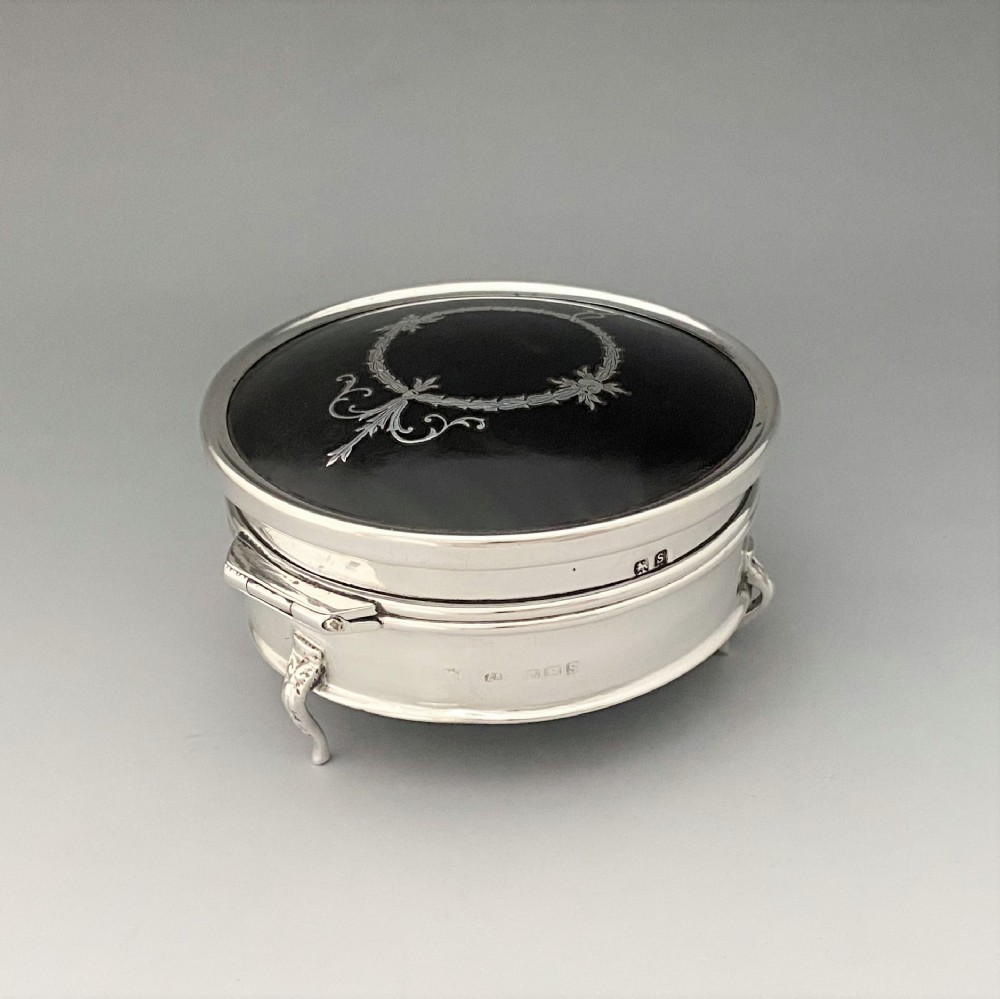 A circular sterling silver trinket box resting on four cabriole legs featuring a dark tortoiseshell lid inlaid with a silver floral garland motif. View III