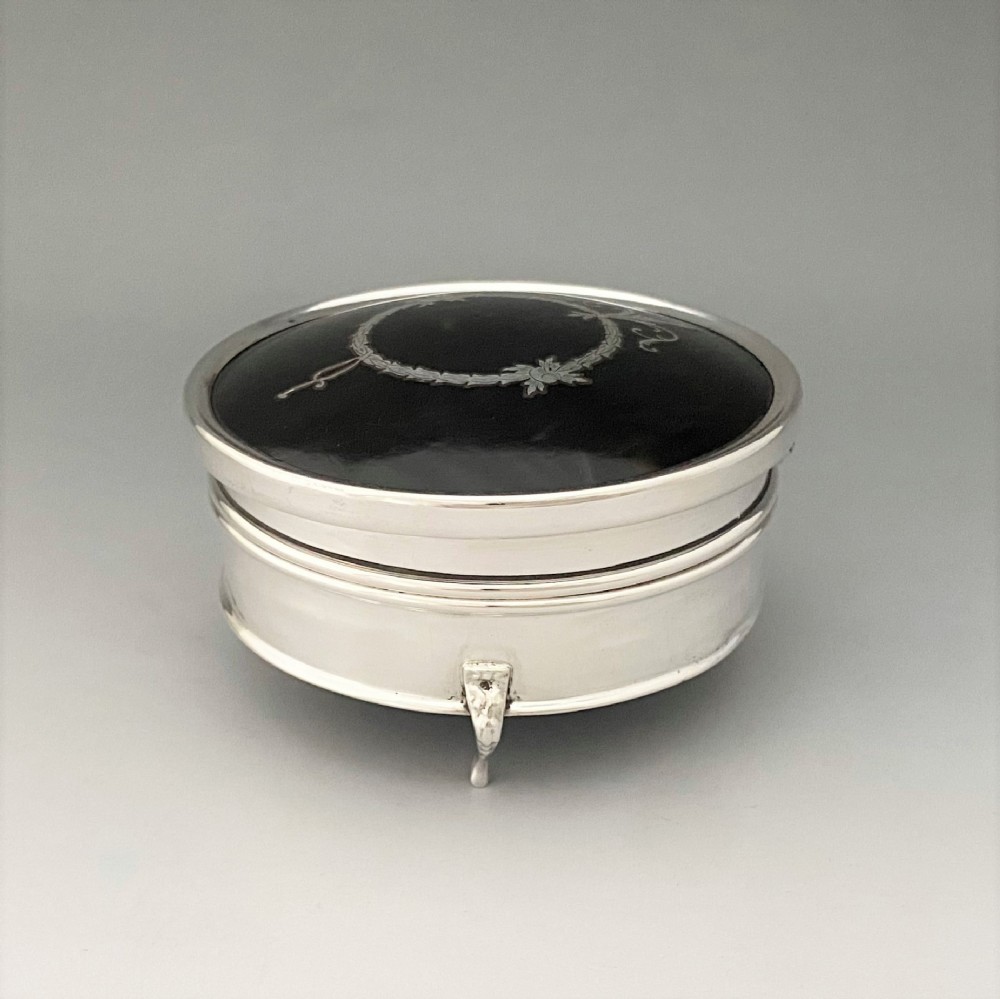 A circular sterling silver trinket box resting on four cabriole legs featuring a dark tortoiseshell lid inlaid with a silver floral garland motif. View IV