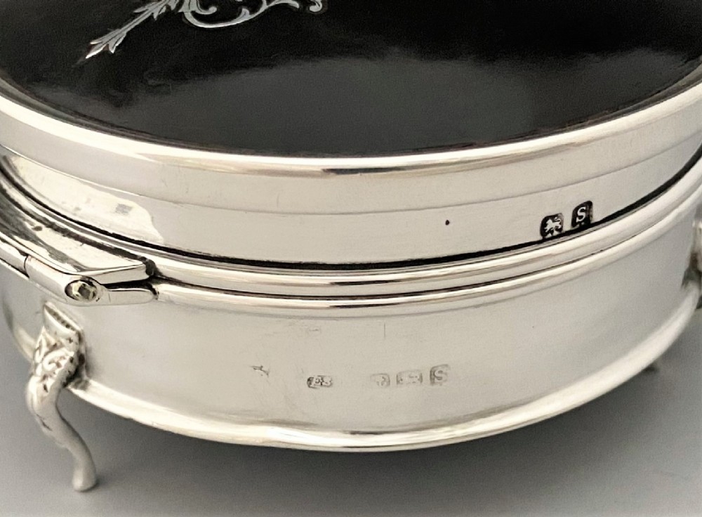 A circular sterling silver trinket box resting on four cabriole legs featuring a dark tortoiseshell lid inlaid with a silver floral garland motif. View VIII