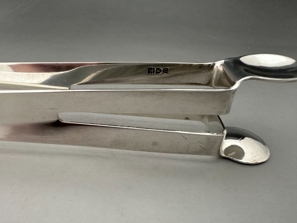 A pair of polished silver Edwardian bar tongs featuring slender arms with mechanical claw gripping ends and flat finger pads. View VI