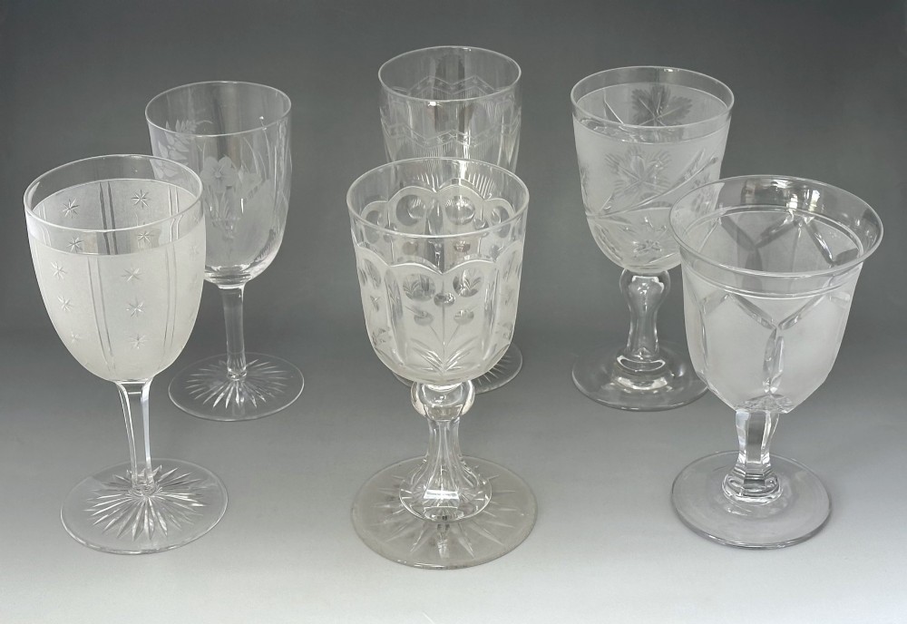A set of six clear Victorian glass goblets, each featuring distinct hand-etched and cut geometric and floral patterns.