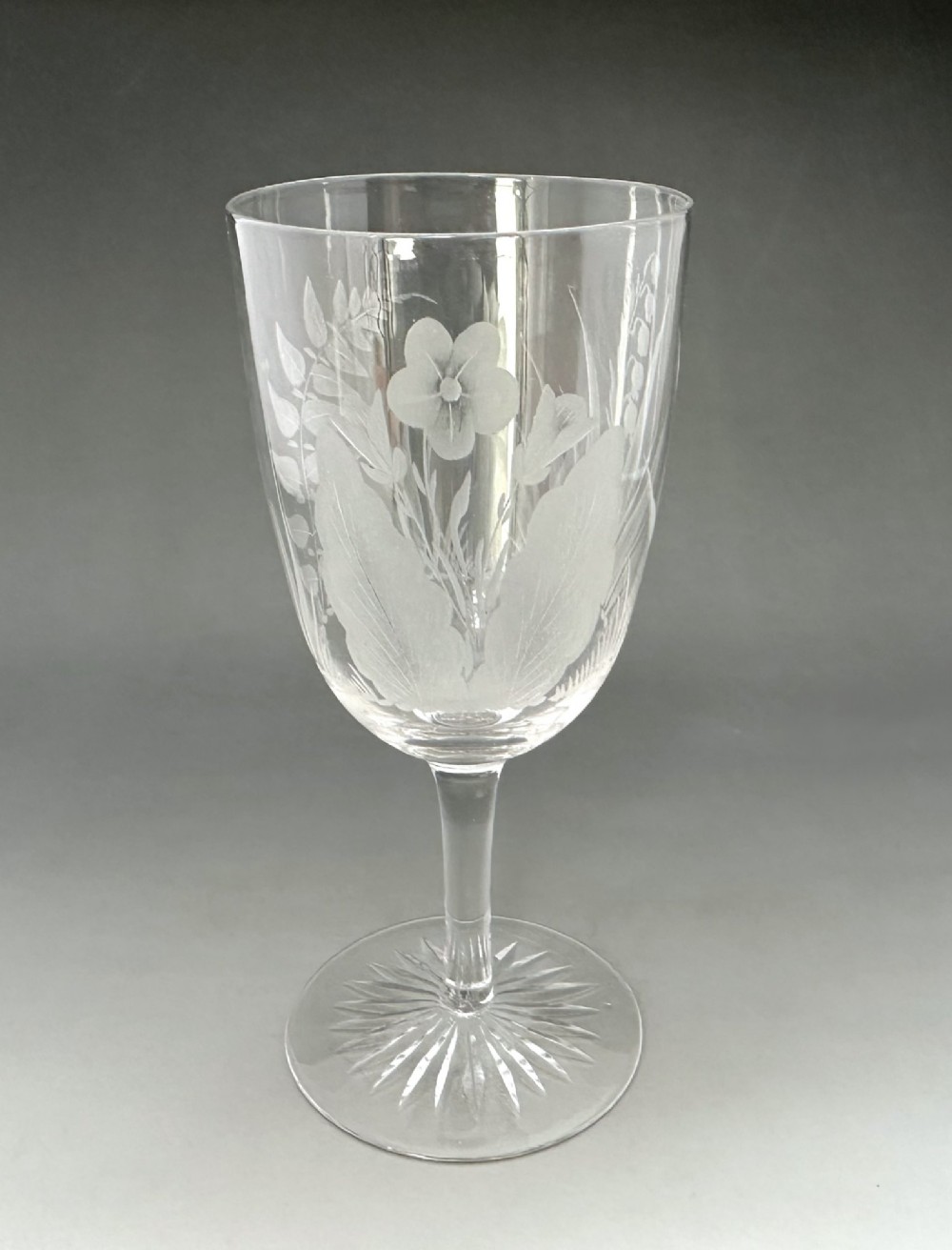 A set of six clear Victorian glass goblets, each featuring distinct hand-etched and cut geometric and floral patterns. View V
