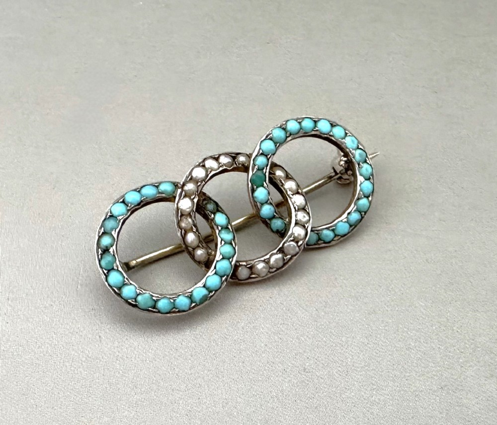 A silver gilt horizontal brooch formed of three interlocking circular rings set with turquoise cabochons and split seed pearls.