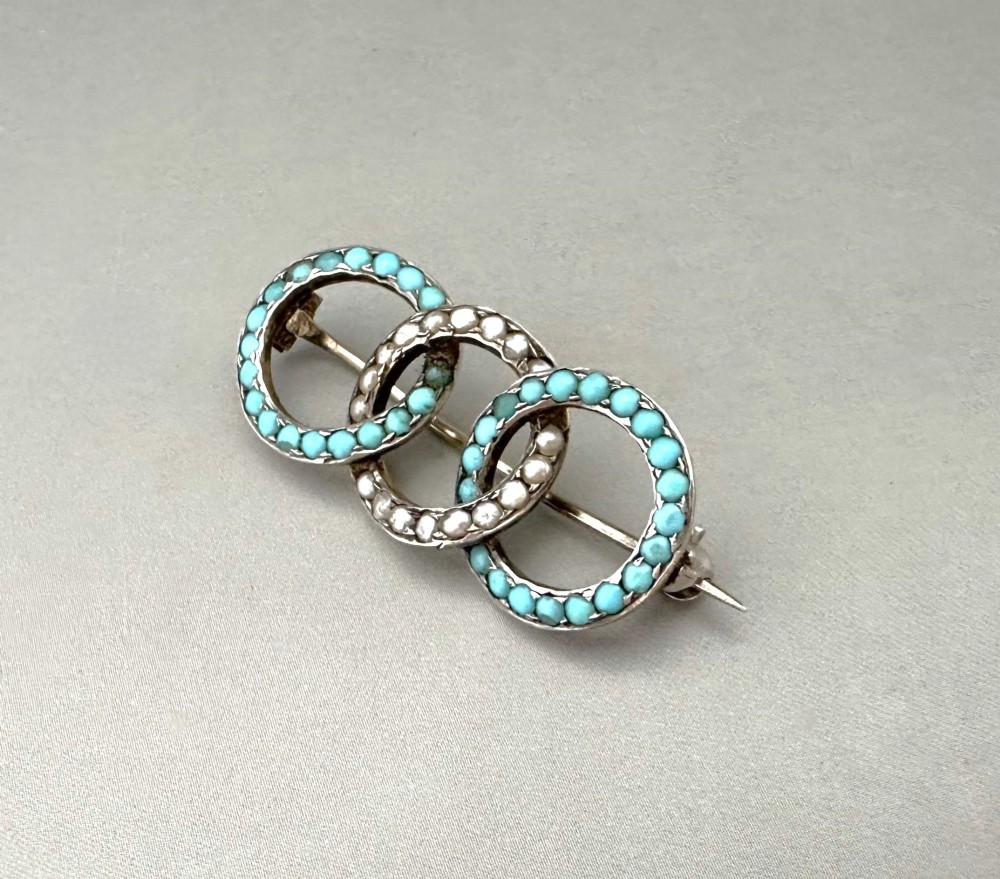 A silver gilt horizontal brooch formed of three interlocking circular rings set with turquoise cabochons and split seed pearls. View II