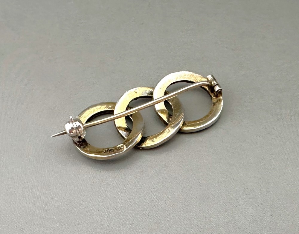 A silver gilt horizontal brooch formed of three interlocking circular rings set with turquoise cabochons and split seed pearls. View III