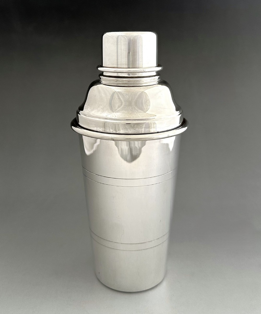 A polished silver-plated three-piece Art Deco cocktail shaker featuring a tapered cylindrical body with incised lines and a stepped cap.