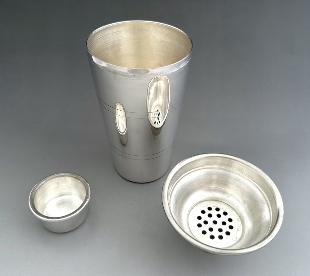 A polished silver-plated three-piece Art Deco cocktail shaker featuring a tapered cylindrical body with incised lines and a stepped cap. View IV