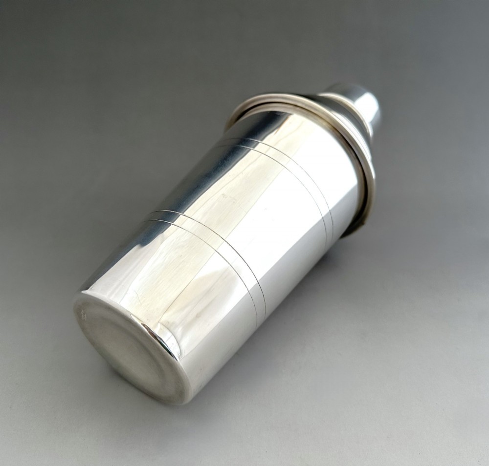 A polished silver-plated three-piece Art Deco cocktail shaker featuring a tapered cylindrical body with incised lines and a stepped cap. View V