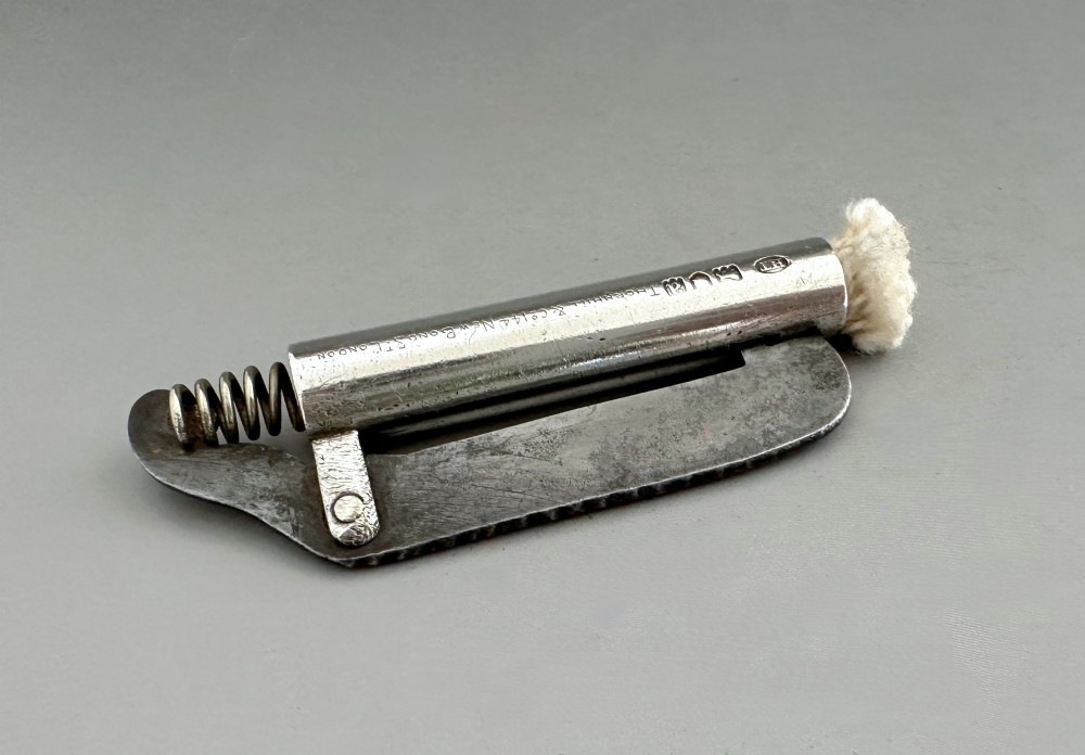 An antique Victorian silver tinder tube with engraved maker details, a steel striker plate, and a protruding cotton wick.