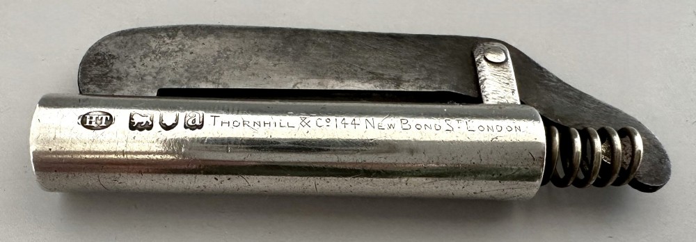 An antique Victorian silver tinder tube with engraved maker details, a steel striker plate, and a protruding cotton wick. View VIII