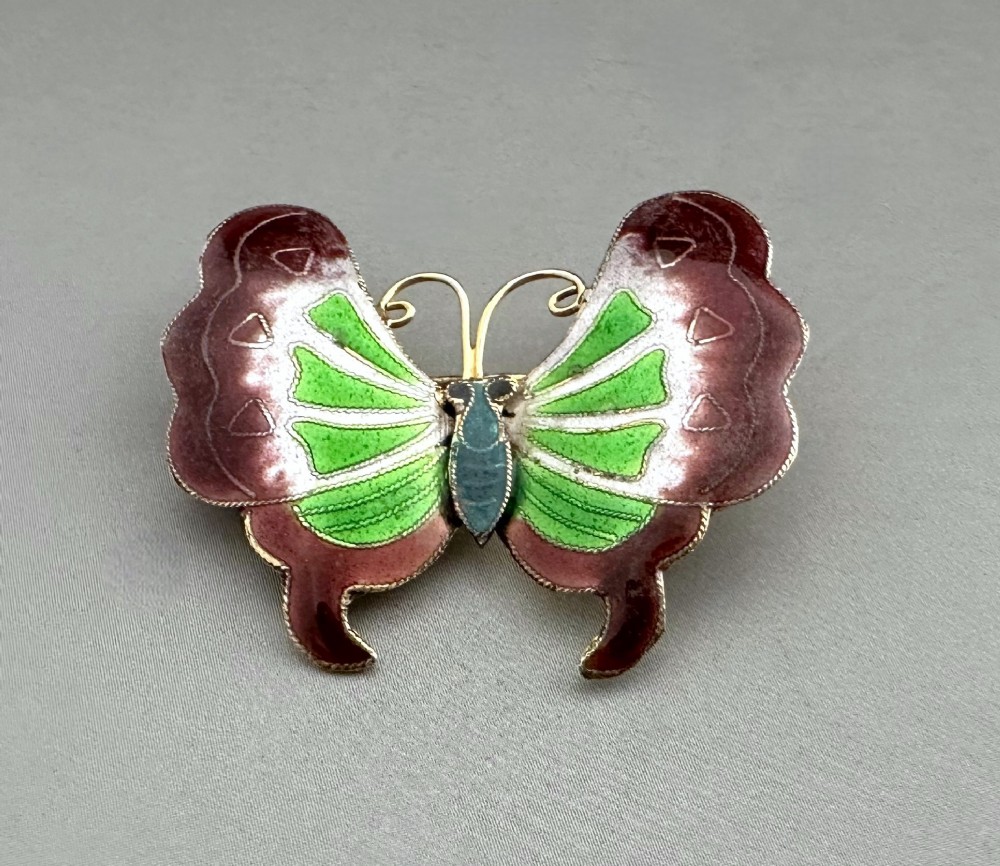 An antique butterfly brooch constructed from silver gilt and detailed with green, white, and burgundy enamel on the wings.