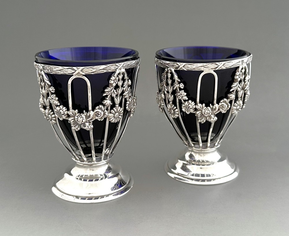 A pair of silver wirework condiment tubs featuring cast floral garlands and cobalt blue glass liners on round pedestal bases. View II