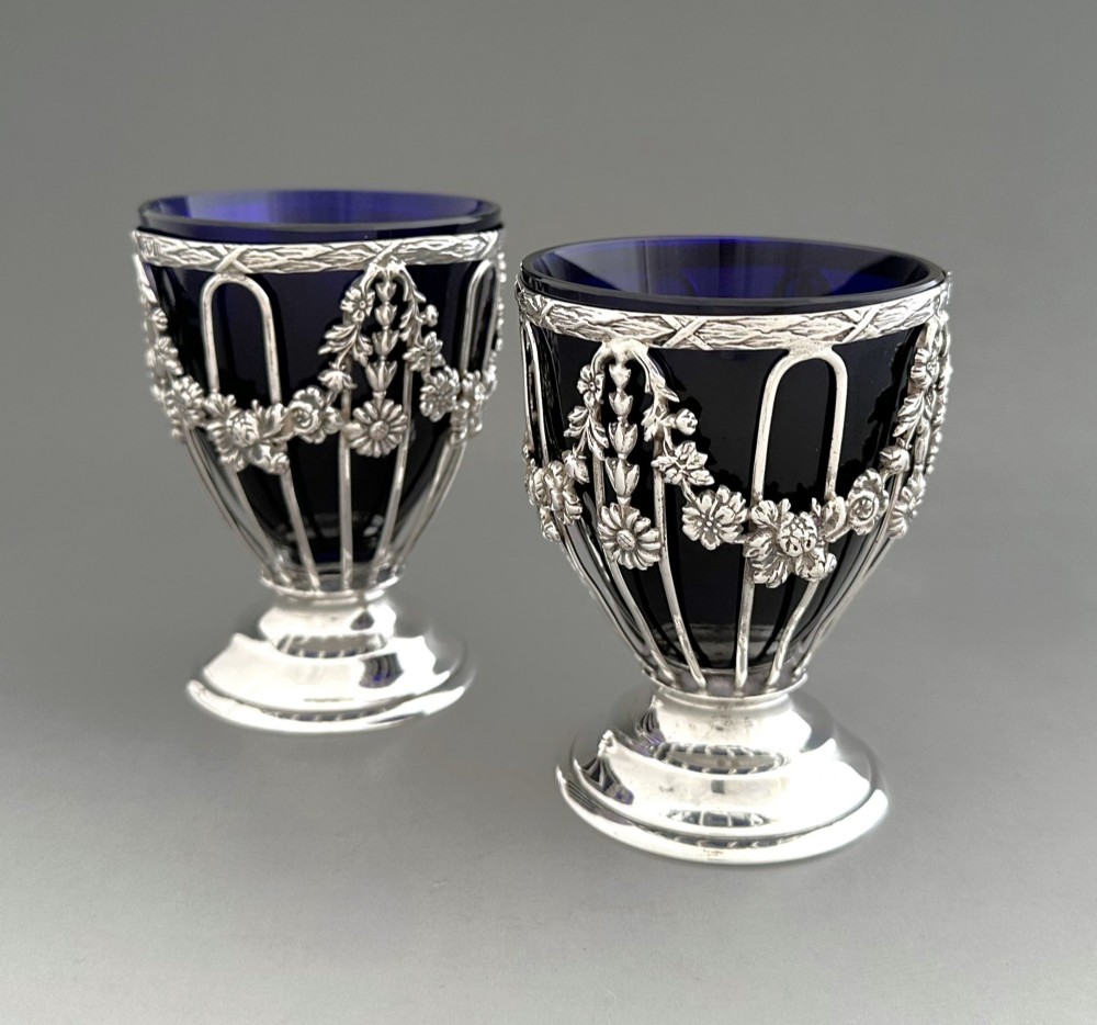 A pair of silver wirework condiment tubs featuring cast floral garlands and cobalt blue glass liners on round pedestal bases. View III
