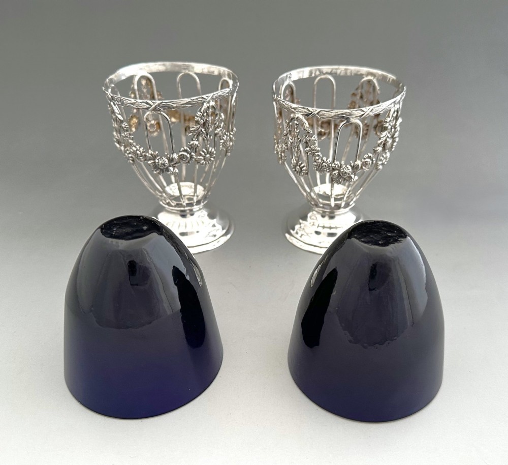 A pair of silver wirework condiment tubs featuring cast floral garlands and cobalt blue glass liners on round pedestal bases. View V