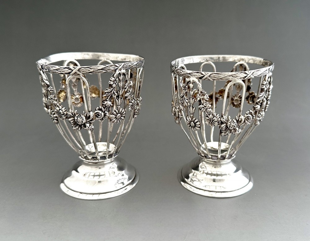 A pair of silver wirework condiment tubs featuring cast floral garlands and cobalt blue glass liners on round pedestal bases. View VI