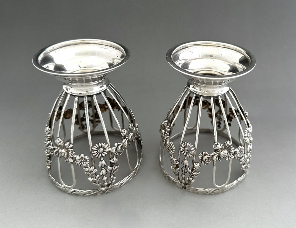 A pair of silver wirework condiment tubs featuring cast floral garlands and cobalt blue glass liners on round pedestal bases. View VII