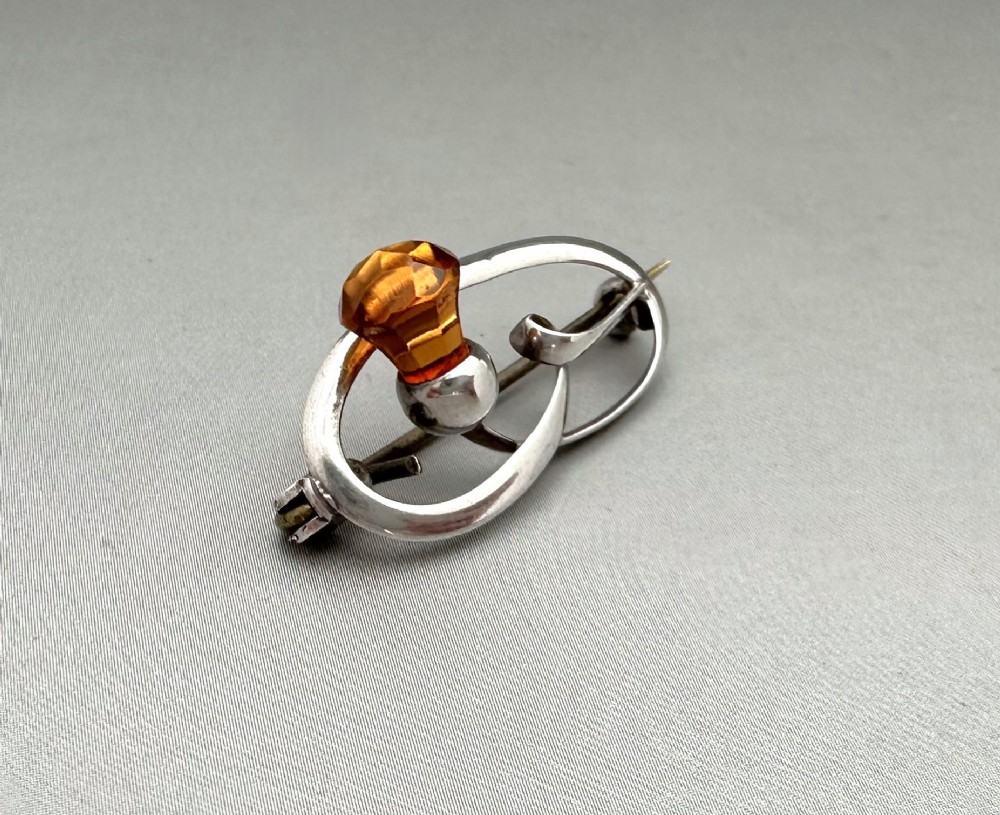 An Art Nouveau silver brooch featuring a stylised oval frame with a central thistle motif topped with a faceted amber-coloured glass stone. View II